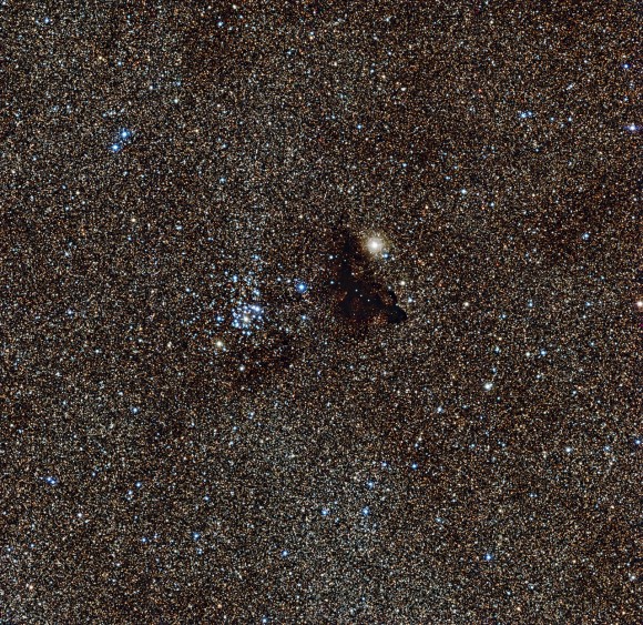 NGC 6520 and its neighbour, the strangely shaped dark cloud Barnard 86. This cosmic pair is set against millions of glowing stars from the brightest part of the Milky Way — a region so dense with stars that barely any dark sky is seen across the picture. Credit: ESO